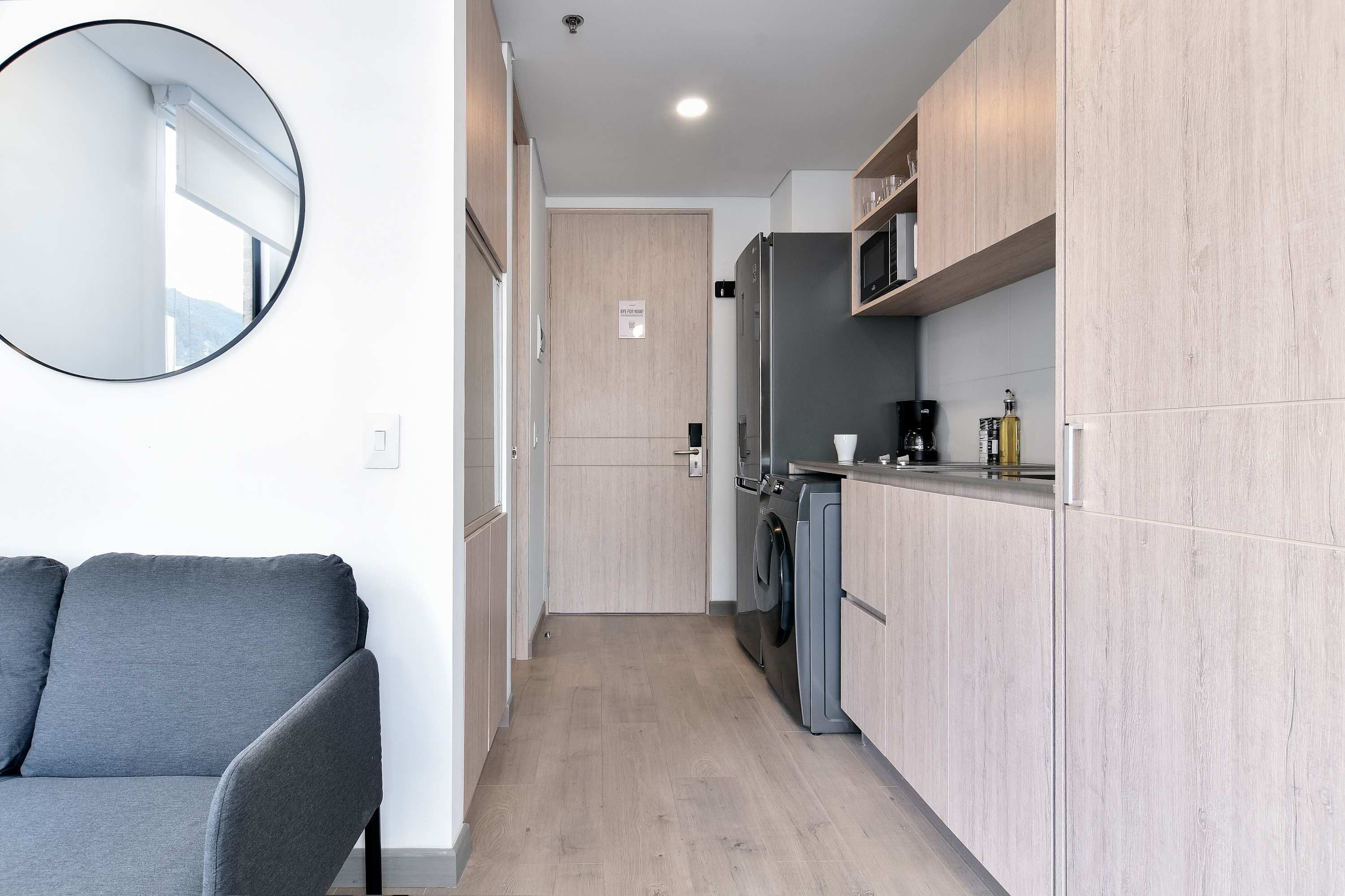 Une cuisine compacte avec des meubles en bois, un lave-linge encastré et un miroir rond accroché au mur.