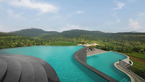 Ein großer, gebogener Infinity-Pool mit Blick auf grüne Hügel und Berge im Hintergrund.