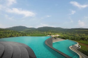 Une grande piscine à débordement aux bords incurvés, offrant une vue sur des collines verdoyantes et des montagnes en arrière-plan.