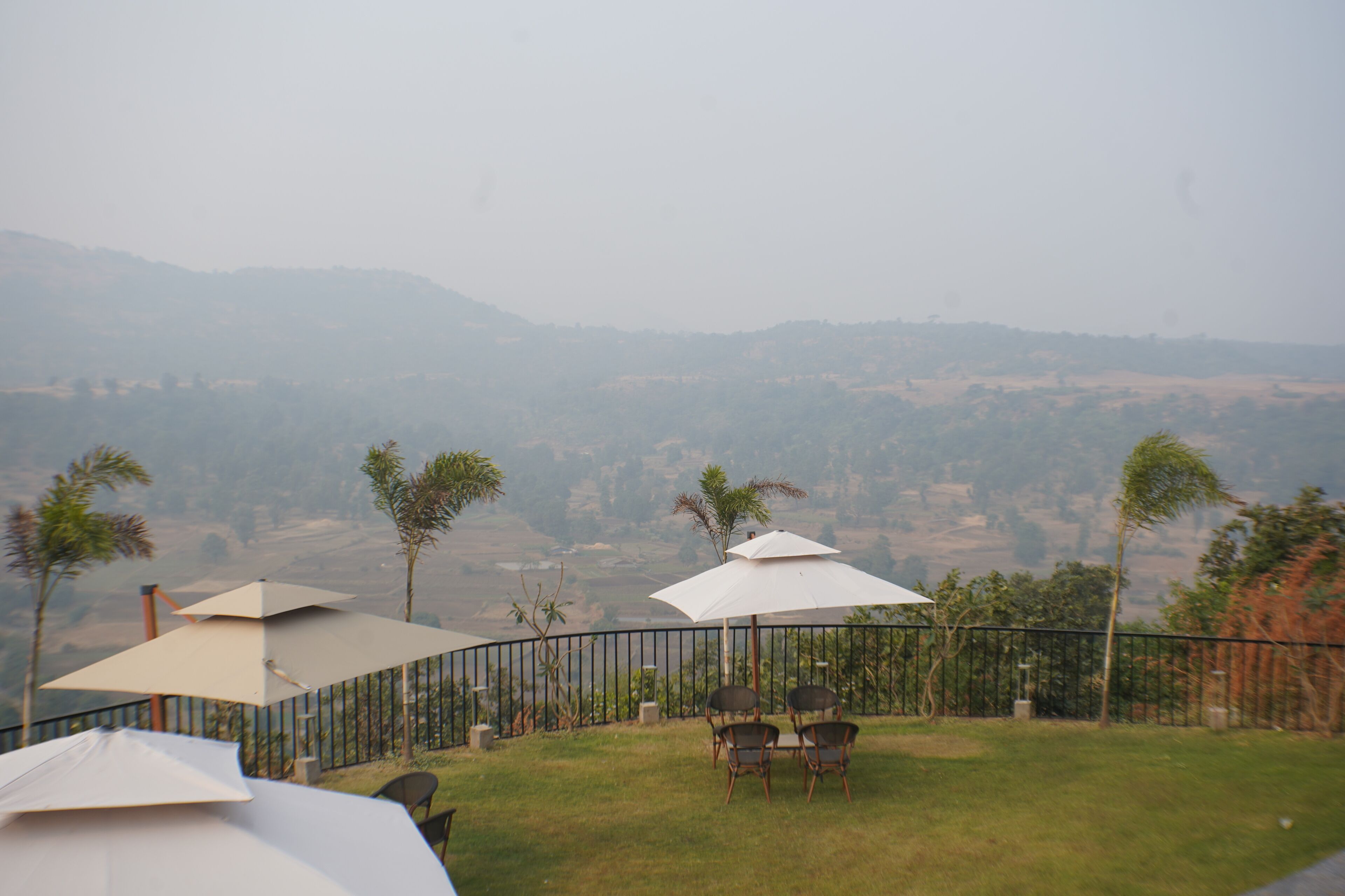 A patio with outdoor seating and umbrellas, overlooking a hilly landscape.