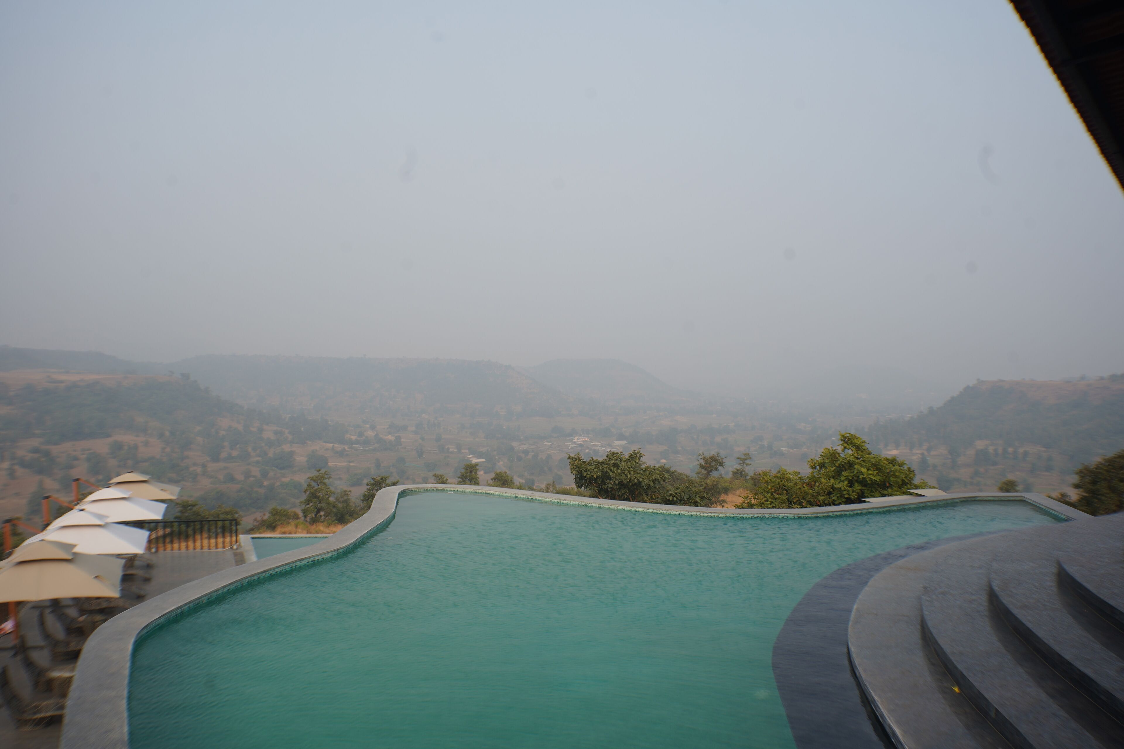 A swimming pool with a curved edge, surrounded by a low wall and a few umbrellas.