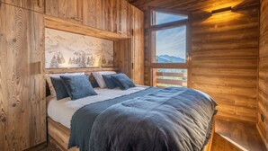 A wooden cabin bedroom with a bed, a mountain view, and a painting on the wall.
