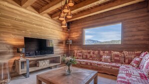 A wooden interior with a sofa, a coffee table, a TV, and a window with a view.