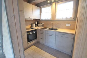 Una cocina compacta con horno integrado, un lavamanos y una ventana sobre la encimera.