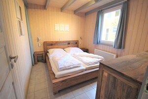 Una habitación de madera con una cama, una mesita de noche, una ventana con cortinas y un radiador.