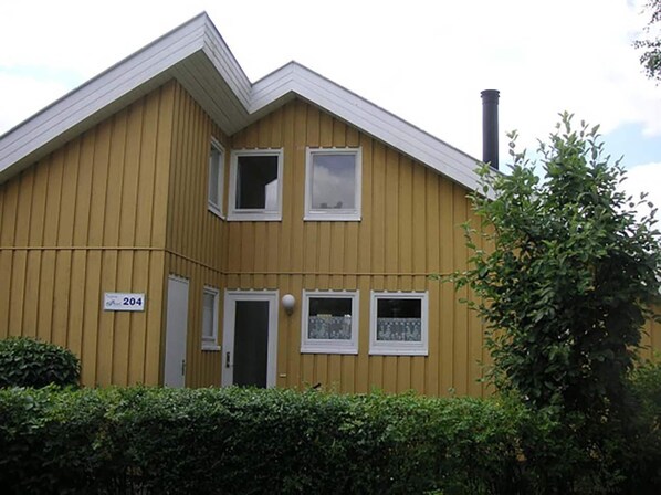 Ein gelbes Gebäude mit zwei Etagen, einem Schornstein, einer Tür und einem Fenster mit Spitzenvorhängen.