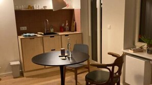Une chambre d’hôtel compacte comprenant un lit, une table de salle à manger ronde avec deux chaises, un coin cuisine et une fenêtre.