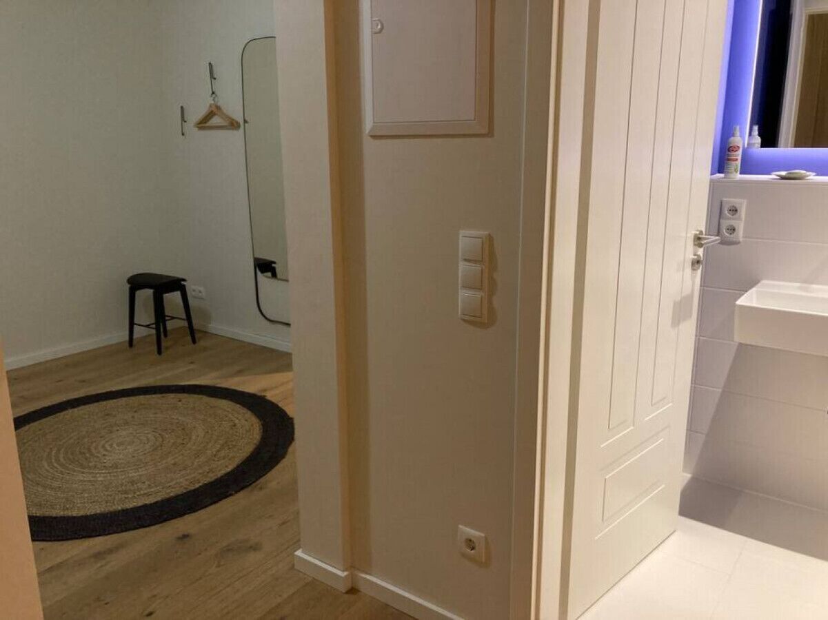 Une pièce avec un plancher en bois, un tapis noir et beige, une porte blanche et un petit tabouret.