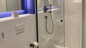 Un baño moderno con cabina de ducha de vidrio, azulejos blancos, lavamanos blanco y espejo con detalles azules.