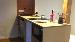A compact kitchen with wooden cabinets, a countertop, and a hanging light fixture. - Arbio I Lax Attic Studio in Lindenau (Leipzig)