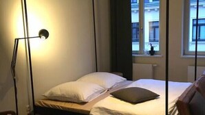 A single bed with a canopy, a bedside table, a lamp, and a view of buildings through a window. - Arbio I Lax Attic Studio in Lindenau (Leipzig)