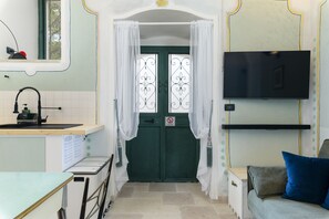 Cocina compacta con lavamanos, una mesita, un armario y una puerta verde con un portón de hierro decorativo.