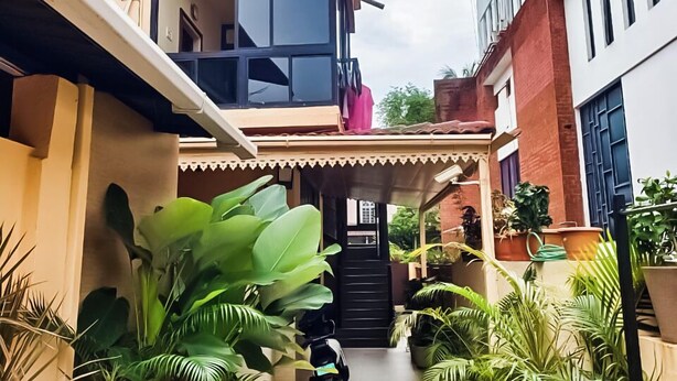 Un étroit sentier bordé de plantes en pot mène à l’entrée d’un bâtiment.