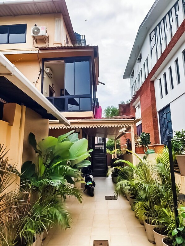 A narrow pathway flanked by potted plants leading to a building entrance. - shradha luxury room (Calangute)