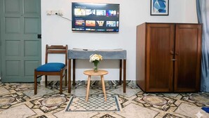 Une pièce avec un téléviseur fixé au mur, un meuble en bois, une chaise bleue, une petite table avec un vase et un revêtement de sol à motifs.