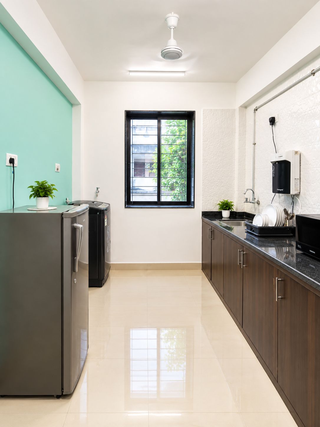 A modern kitchen with a stainless steel refrigerator, a built-in oven, a microwave, and a sink. There is a window with a view of greenery outside.