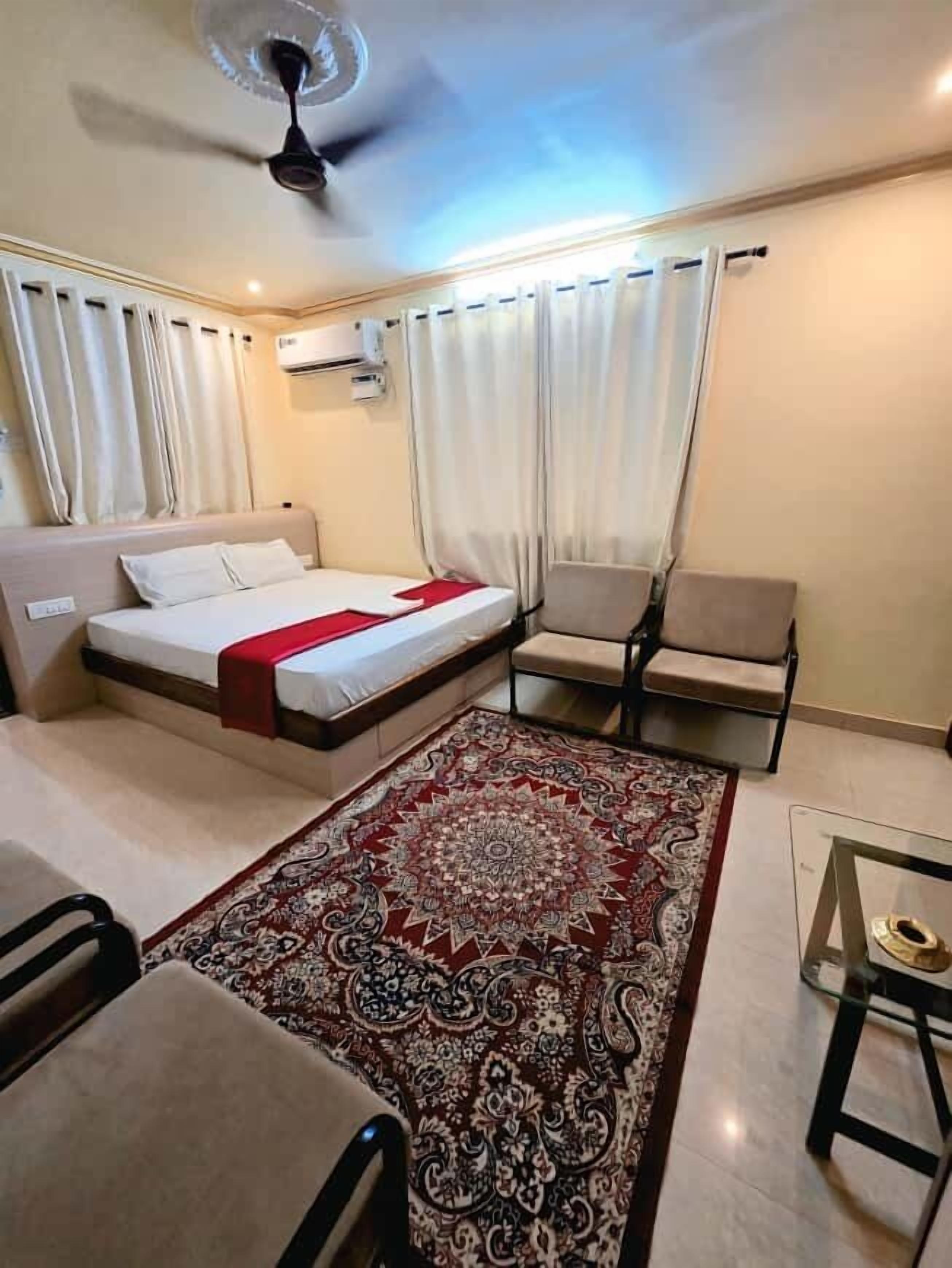 A hotel room with a bed, two chairs, a small table, a ceiling fan, and a patterned rug.
