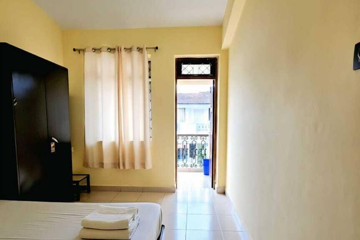 A hotel room with a bed, a wardrobe, a ceiling fan, a window with curtains, and a view of the outside balcony.