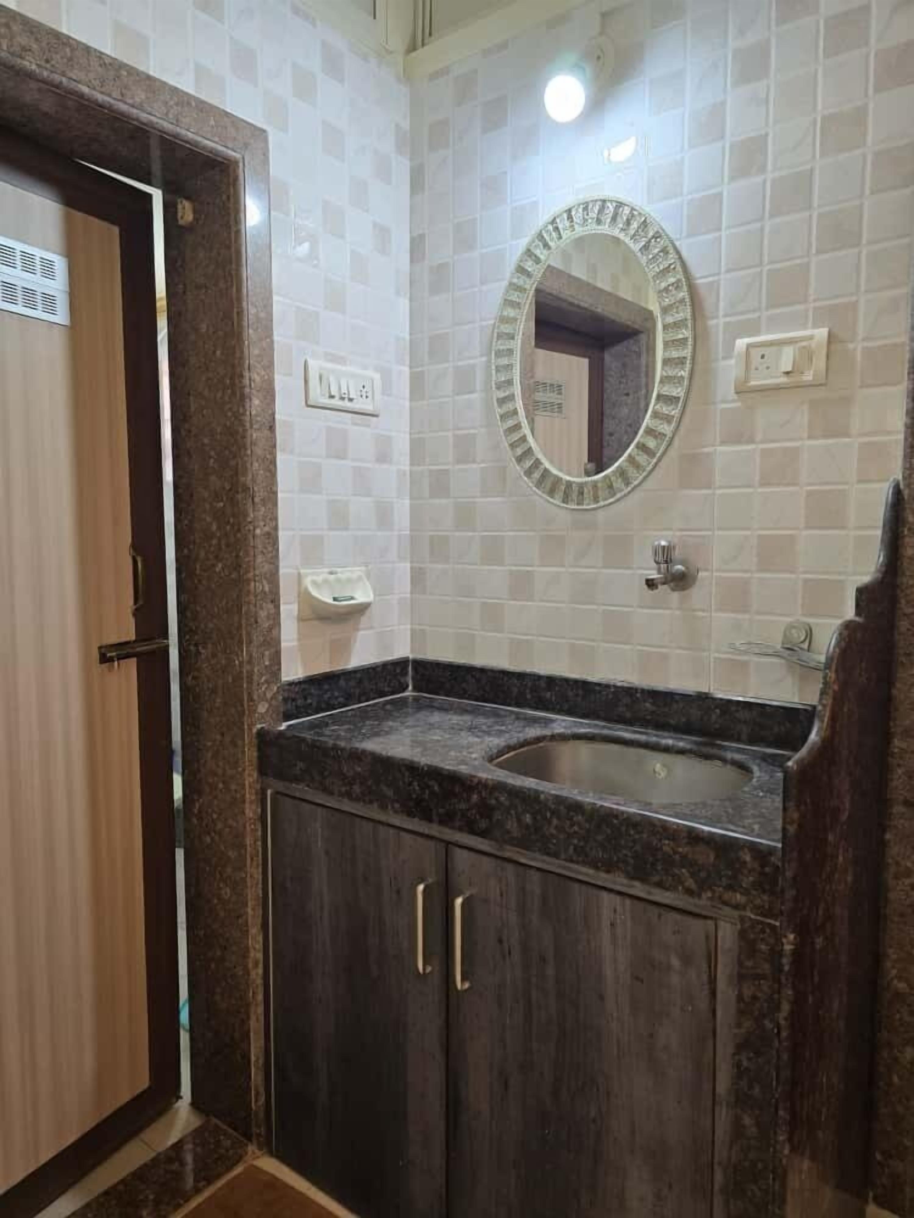 A bathroom with a double sink, dark wood cabinets, a marble countertop, a mirror with a decorative frame, and a tiled wall.