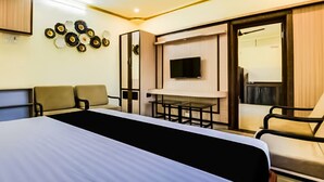 Une chambre d’hôtel avec un lit, deux fauteuils, une télévision et un miroir.