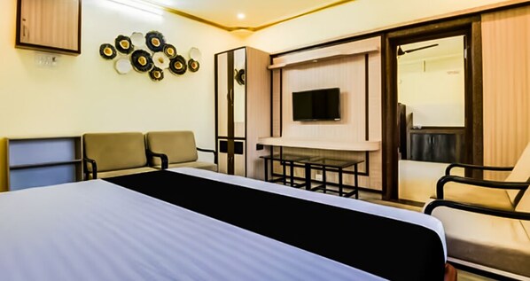 Habitación de hotel con una cama, dos sillones, un televisor y un espejo.