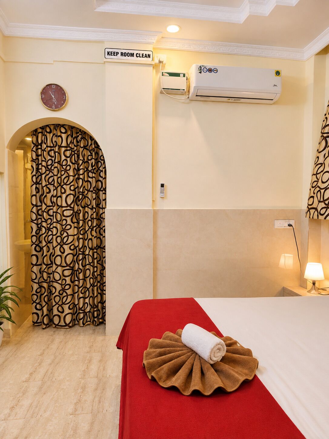 Habitación de hotel con una cama, un reloj de pared, equipo de aire acondicionado, un cartel que indica mantener la habitación y una cortina estampada.