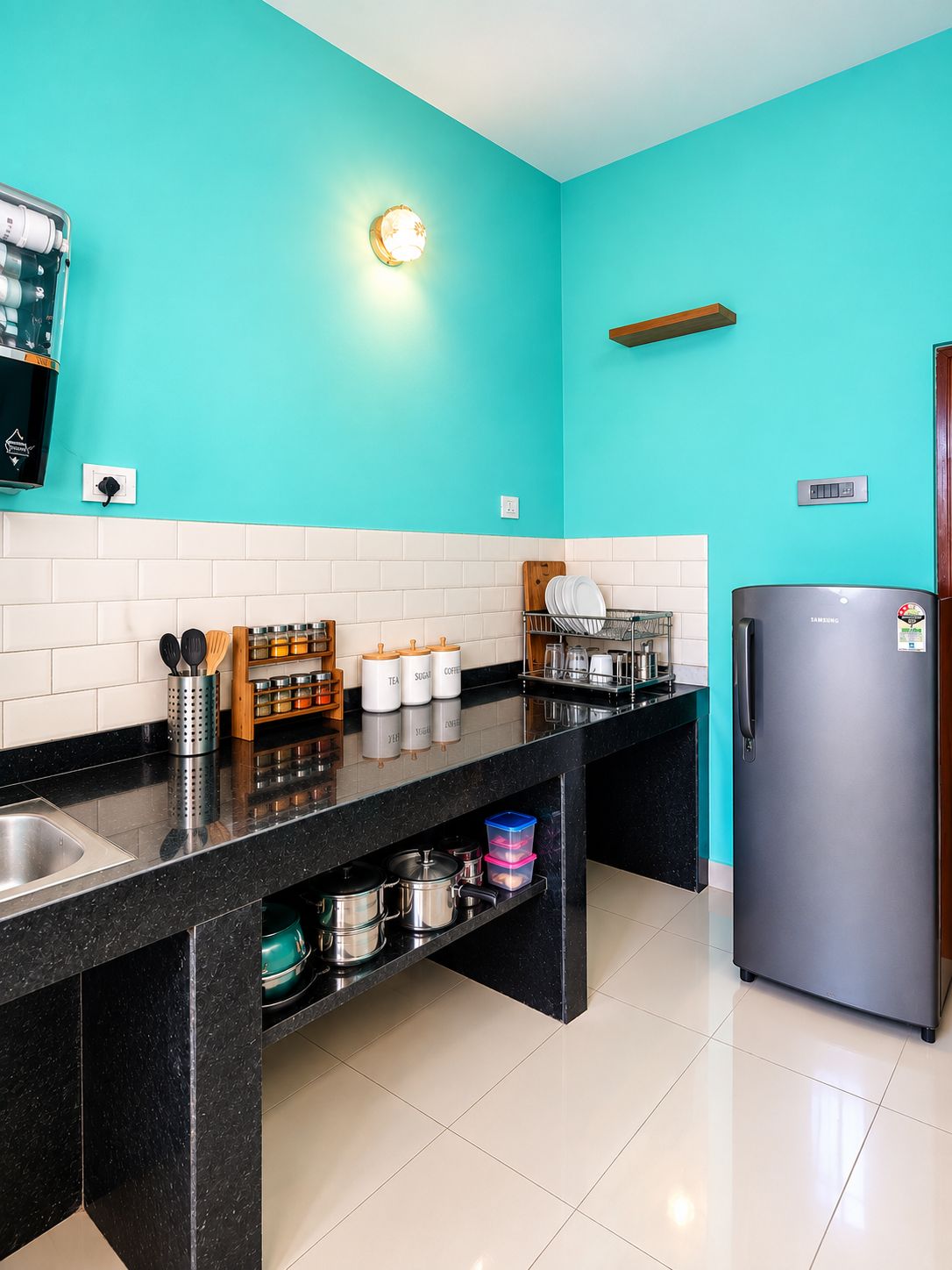 A kitchen with a teal wall, a stainless steel refrigerator, and a black countertop.