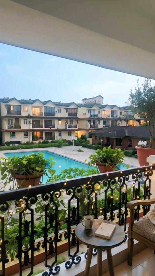 Een balkon met uitzicht op een zwembad en een meer verdiepingen tellend gebouw op de achtergrond.