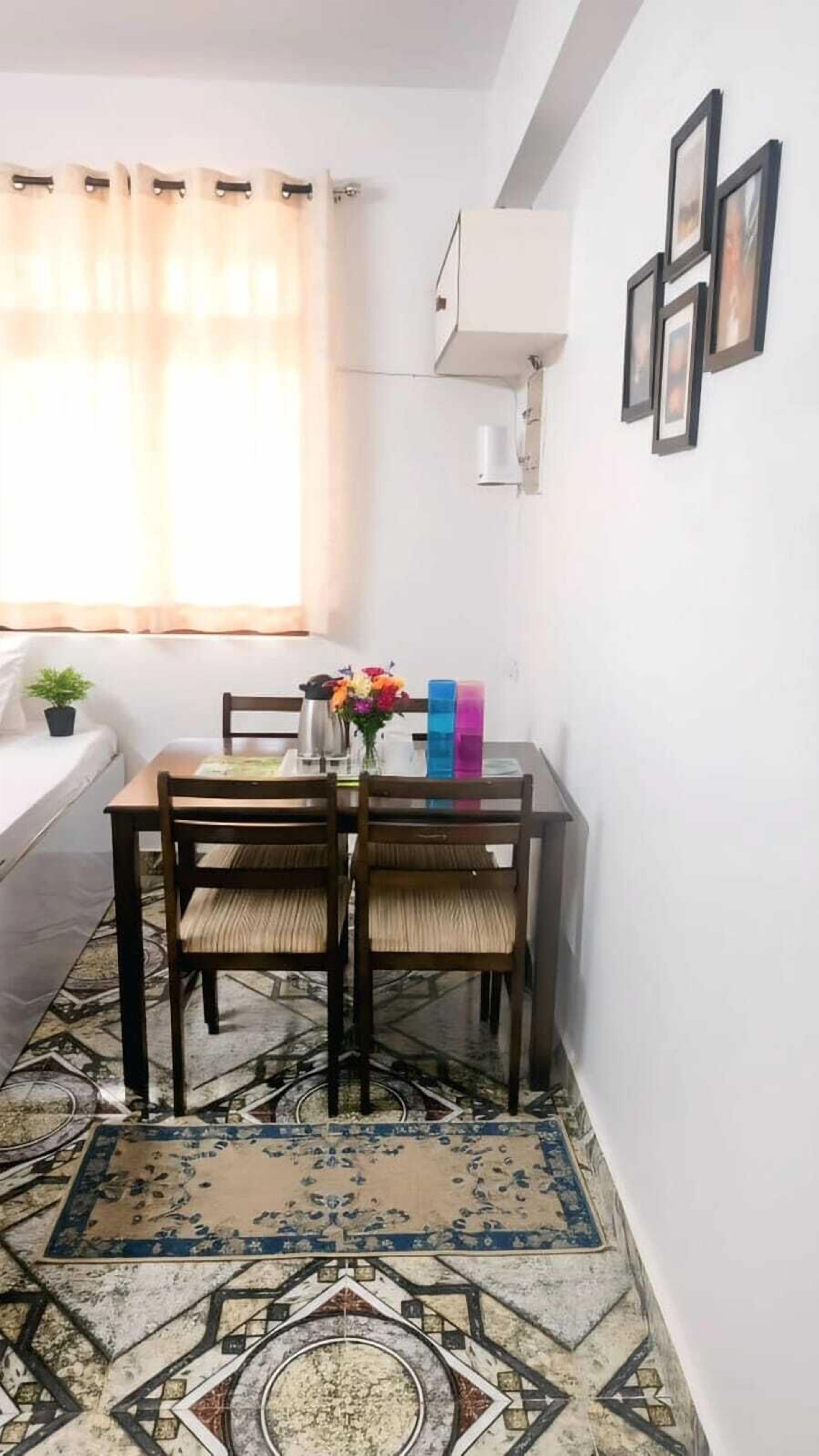 Un pequeño comedor con una mesa, sillas, una planta en maceta y un florero colorido.