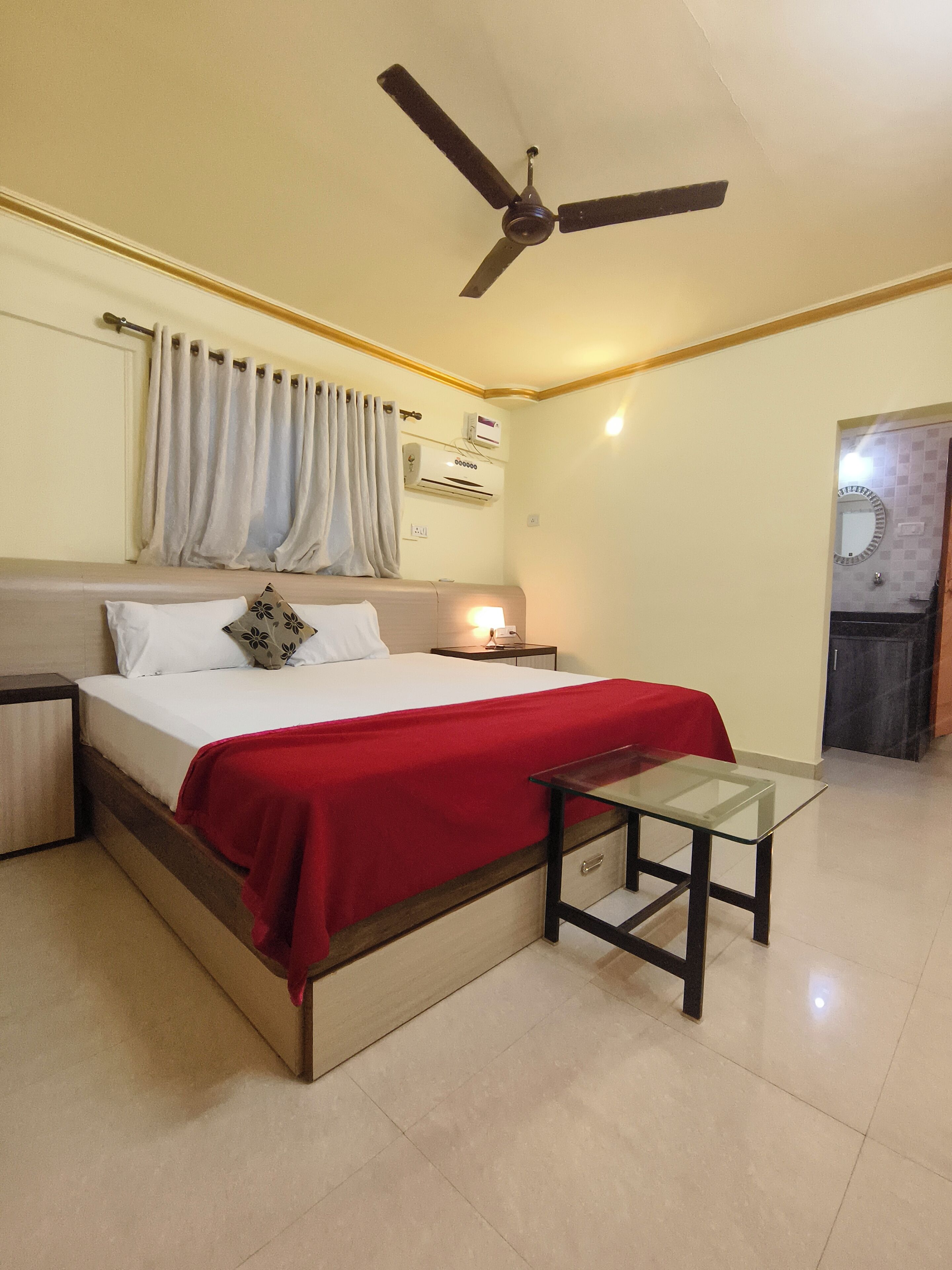 Un dormitorio con cama, mesita de noche, mesa, ventilador de techo y aire acondicionado.