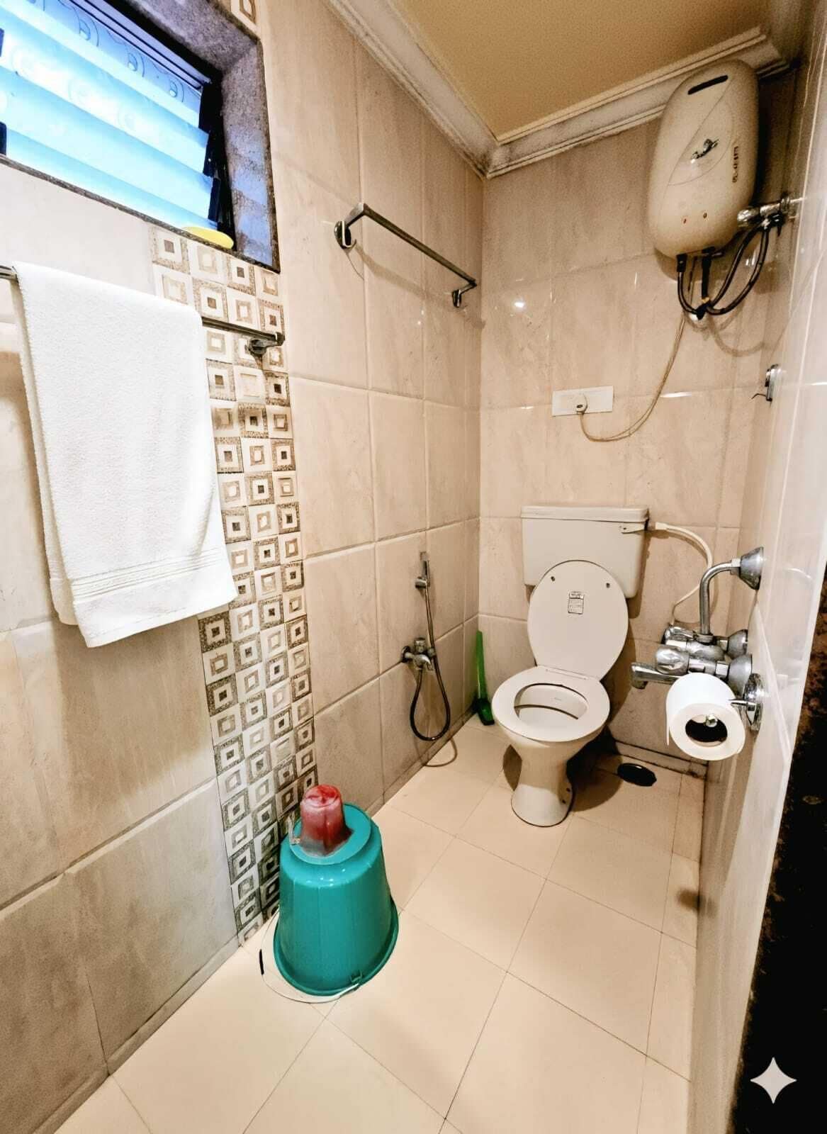 Une petite salle de bain comprenant des toilettes, une douche et un lavabo. On y trouve également un porte-serviettes et un support à papier toilette.