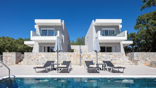 Un espace moderne aménagé au bord de la piscine, avec deux bâtiments blancs, des murs en pierre et des chaises longues.