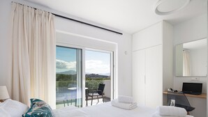 Une chambre d’hôtel moderne avec un grand lit, un balcon avec une chaise, un ordinateur portable sur un bureau et une vue sur l’extérieur.