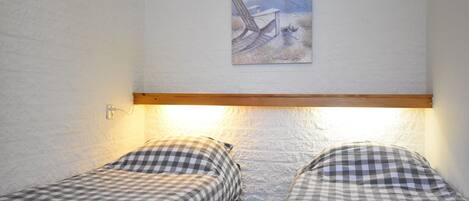 Een kamer met twee bedden, elk met geruit beddengoed, en een schilderij van een strandtafereel boven de bedden. Daarboven loopt een houten balk.