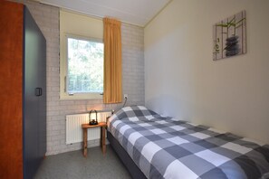 Un dormitorio con cama, una ventana con cortinas, un radiador y una mesita.