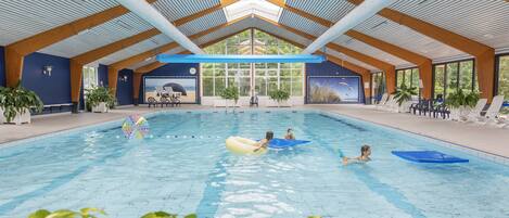 An indoor swimming pool with a high ceiling, wooden beams, and large windows.
