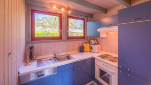 A compact kitchen with wooden walls, a sink, a stove, and two windows with red frames. - Exklusives Skandinavisches Ferienhaus (Mirow)