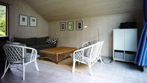 A room with a sofa, two white wicker chairs, a wooden coffee table, a white cabinet, and framed pictures on the wall. - Exklusives Skandinavisches Ferienhaus (Mirow)
