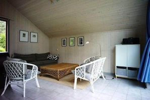 A room with a sofa, two white wicker chairs, a wooden coffee table, a white cabinet, and framed pictures on the wall. - Exklusives Skandinavisches Ferienhaus (Mirow)