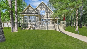 A two-story house with a front porch, surrounded by a well-maintained lawn and tall trees.