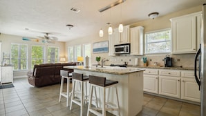 A spacious kitchen with a central island, white cabinets, and a large window.