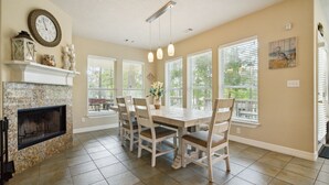 A dining area with a fireplace, a clock, and a window with blinds.