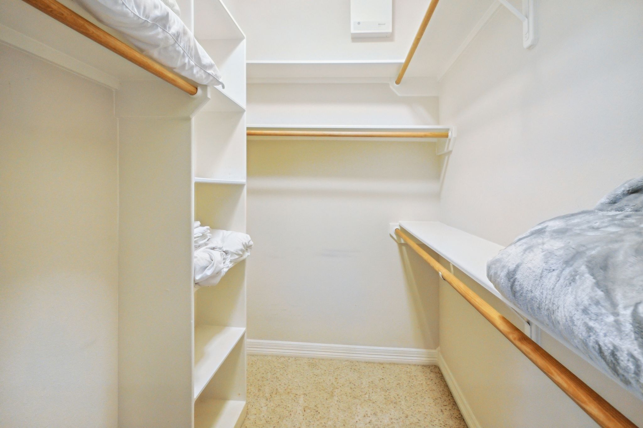 Un petit dressing étroit avec des étagères en bois et un lit recouvert d’une couverture grise.