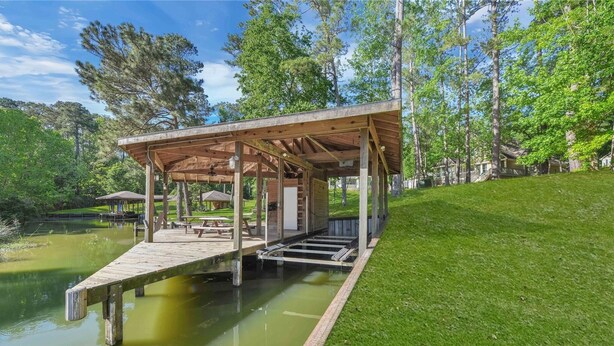 A wooden dock extending over a pond with a covered seating area and a small pavilion nearby.