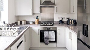 Une cuisine moderne avec des meubles blancs, une hotte en acier inoxydable, un four encastré et un réfrigérateur.