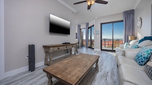 Una sala moderna con televisión de pantalla plana, una mesa de centro de madera, un sofá con cojines estampados y un balcón con vistas.