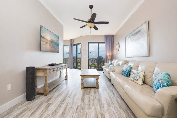 A spacious living room with a sofa, coffee table, and a dining area with a wooden table and chairs. - Phoenix X 102 1 Bedroom Condo (Orange Beach)