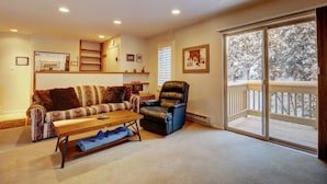 A living room with a sofa, a coffee table, a chair, and a large window with a view of trees.