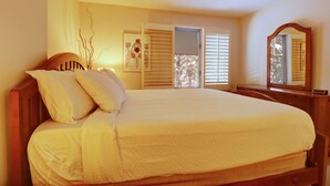 A bedroom with a large bed, a wooden headboard, a nightstand, a dresser, and a mirror.