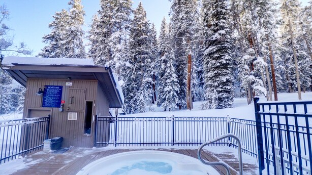 A wooden deck with a hot tub surrounded by snow-covered trees.